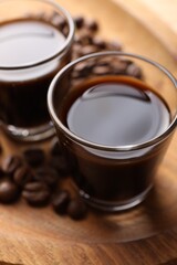 Shot glasses with coffee liqueur and beans on wooden tray, closeup