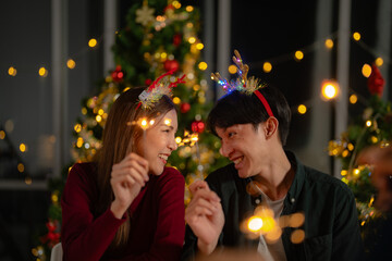 man and woman holding sparkler fireworks in a party with Christmas tree. young couple Asian people enjoy celebrating Christmas and New Year. happy and celebrate with food wine and friendship for love,