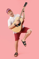 Male hippie playing guitar on pink background