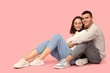 Happy young couple sitting on floor and hugging against pink background