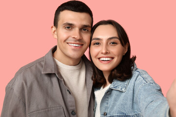 Happy young couple taking selfie on pink background