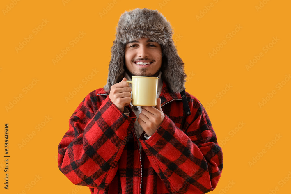 Canvas Prints Young man in winter clothes with cup of hot tea on yellow background