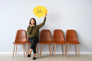 Asian businesswoman holding speech bubble with word JOB near light wall