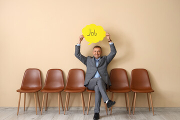 Mature businessman holding speech bubble with word JOB near beige wall