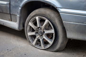 A flat tire or tear rubber tire of an old abandoned broken car on the city parking. The old rubber vehicle tire. Automobile junkyard or car dump. Scrap and recycling vehicle. Environmental problems