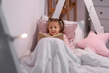 Cute little girl reading story in bedroom at night