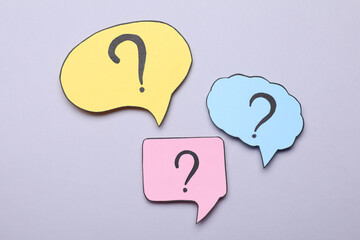 Different paper speech bubbles with question marks on light grey background, flat lay