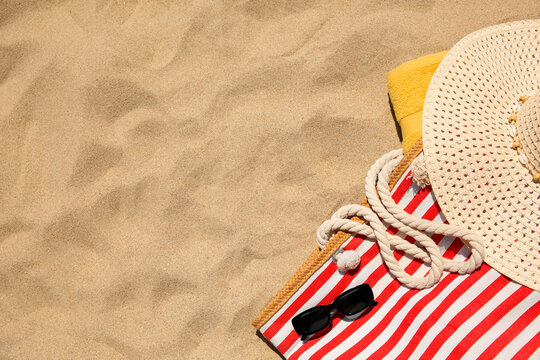 Striped beach bag, sunglasses, towel and hat on sand, flat lay. Space for text