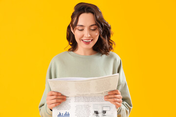 Young woman reading newspaper on yellow background