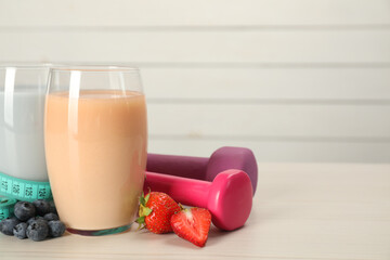 Tasty shakes with berries, dumbbells and measuring tape on wooden table, space for text. Weight loss - Powered by Adobe