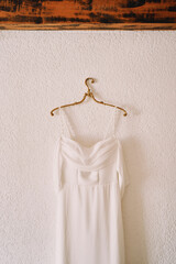 Wedding dress with straps hanging on a hanger on a white wall