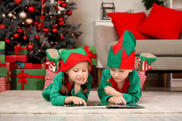 Cute little children in elf costumes reading story at home on Christmas eve