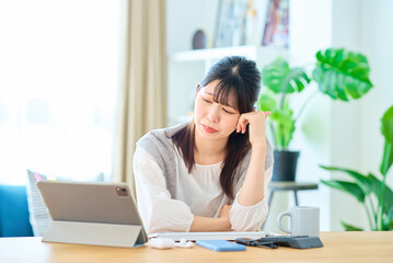 部屋でパソコン作業をしながら疲れた表情の若い女性