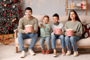 Fototapeta premium Happy family with popcorn watching Christmas movie on TV at home