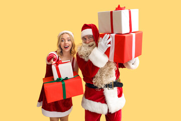 People dressed as Santa Claus with Christmas gifts pointing at viewer on yellow background
