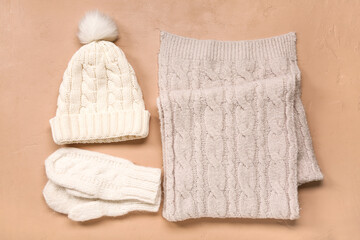 Pair of knitted mittens with warm hat and scarf on beige background