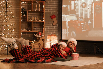 Young couple with popcorn watching Christmas movie on projector screen at home