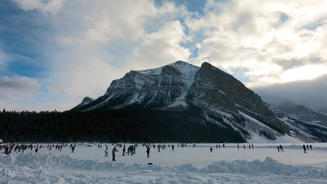 people skating on frozen Lake Louise with a huge mountain in background in cloudy day sunset time. tourism in Alberta. winter holiday season. Christmas holiday season. peaceful nature in Canada.
