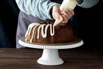 Hands piping buttercream frosting onto a chocolate bundt cake.