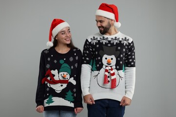 Young couple in Christmas sweaters and Santa hats on grey background