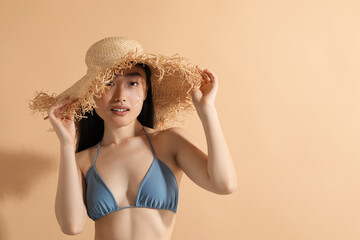 Beautiful young woman in straw hat with sun protection cream on her face against beige background, space for text