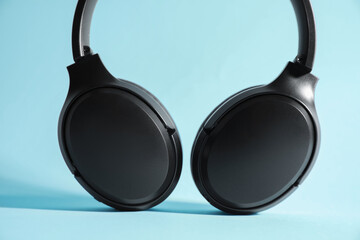 Modern wireless headphones on light blue background, closeup