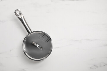 One steel saucepan with strainer lid on white marble table, top view. Space for text