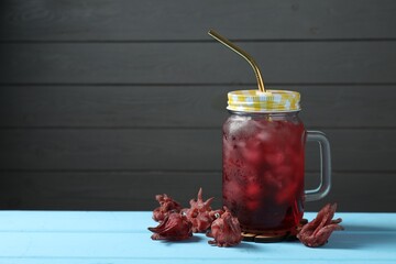 Mason jar of delicious iced hibiscus tea and dry flowers on light blue wooden table, space for text © New Africa