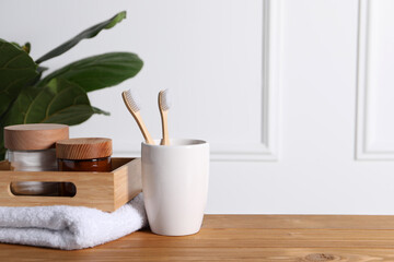 Fototapeta na wymiar Bamboo toothbrushes in holder, towel, cosmetic products and leaves on wooden table. Space for text