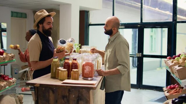 Merchant presenting organic items to vegan customer shopping for groceries, showing sauces and pantry goods in containers. Client thinking about buying fresh natural food produce.