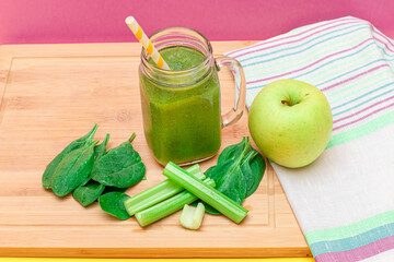 Fresh Green Smoothie of Apple, Celery, and Spinach in Glass Smoothie Jar with Yellow Cocktail Straw on Wooden Cutting Board. Vegan Detox Drink. Vegetarian Culture. Healthy Eating and Fruit Diet