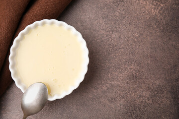 Bowl with condensed milk and spoon on brown table, top view. Space for text