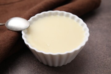 Bowl with condensed milk and spoon on brown table, closeup