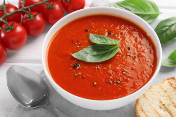 Delicious tomato cream soup in bowl served on white wooden table, closeup