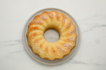 Delicious freshly baked sponge cake on white marble table, top view