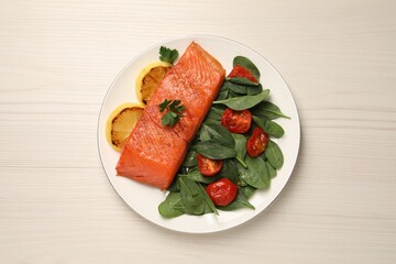 Tasty grilled salmon with basil, tomatoes and lemon on white wooden table, top view