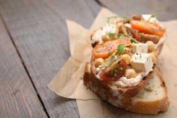 Tasty vegan sandwich with tomatoes, tofu and chickpeas on wooden table, closeup. Space for text