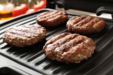 Delicious hamburger patties cooking on electric grill, closeup