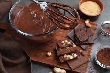 Bowl of chocolate cream, whisk and ingredients on table, closeup
