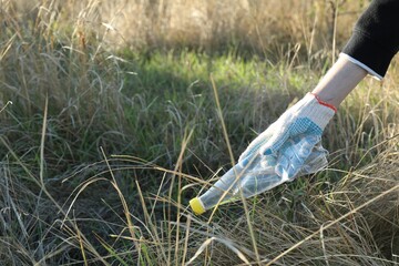 Woman picking up plastic bottle outdoors, closeup. Space for text