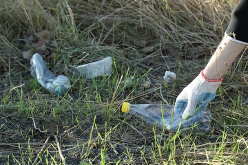 Woman picking up plastic bottle outdoors, closeup. Space for text