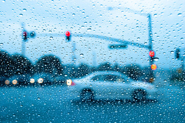 Raindrops in focus on a windshield. with an intersection and a car diffused in the background