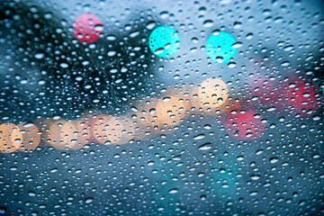 Raindrops in focus on a windshield. with an intersection and colorful bokeh diffused in the background