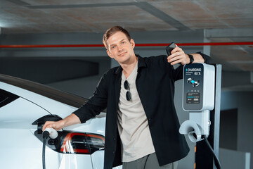 Young man travel with EV electric car to shopping center parking lot charging in downtown city...