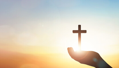 human hand holding the Jesus Christ cross on sunset sky background.