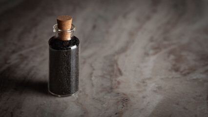 A small glass bottle filled with organic Organic black cumin  (Nigella sativa) or kalonji is placed on a marble background.