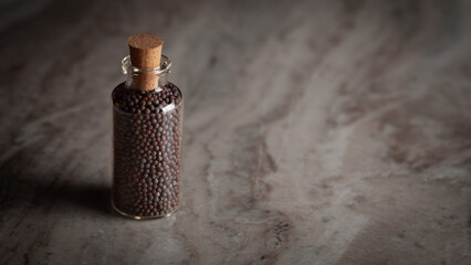 A small glass bottle filled with organic Black mustard seed (Brassica nigra) is placed on a marble...