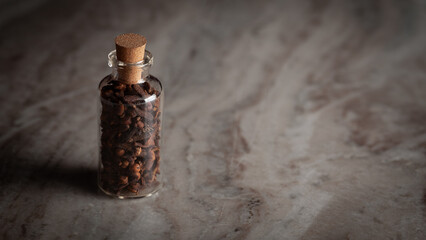 A small glass bottle filled with organic Clove (Syzygium aromaticum) or Indian long is placed on a marble background.
