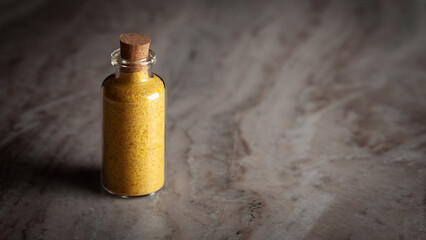 A small glass bottle filled with organic Heeng (Asafoetida) is placed on a marble background.