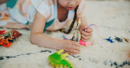 Girl child, dinosaur toys and floor with playing, development and relax with game in room at family...